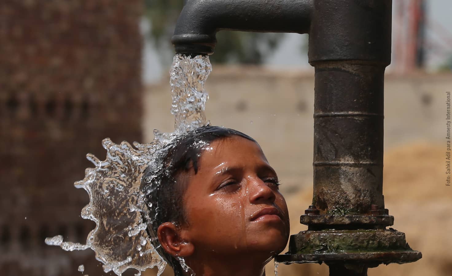 Un niño se refresca con una bomba manual de agua